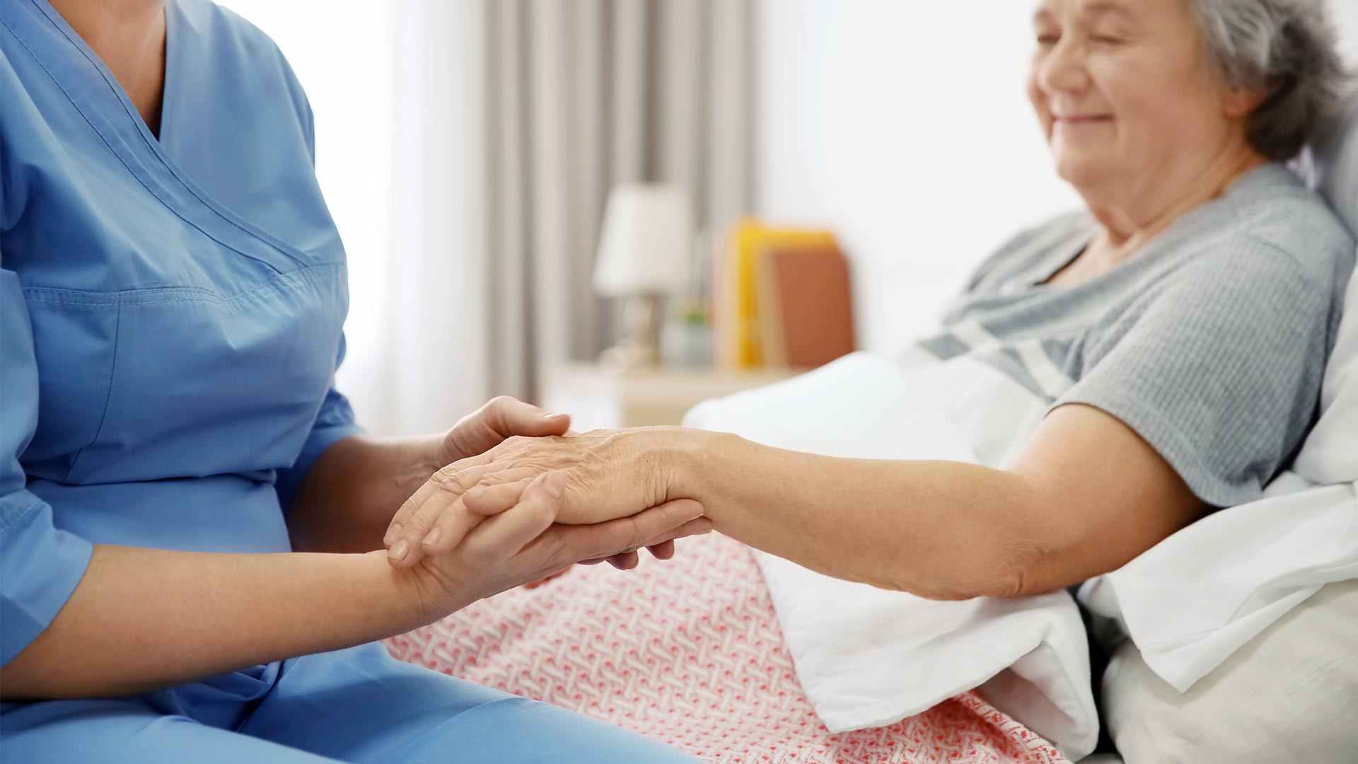 Nurse holding patient's hand in bed